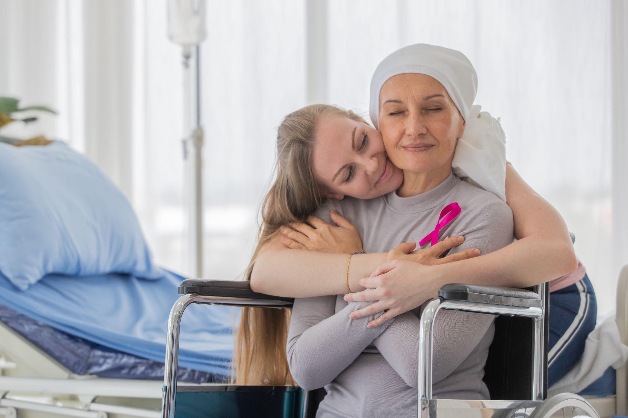 A woman hugging a cancer patient who is wearing a pink cancer ribbon